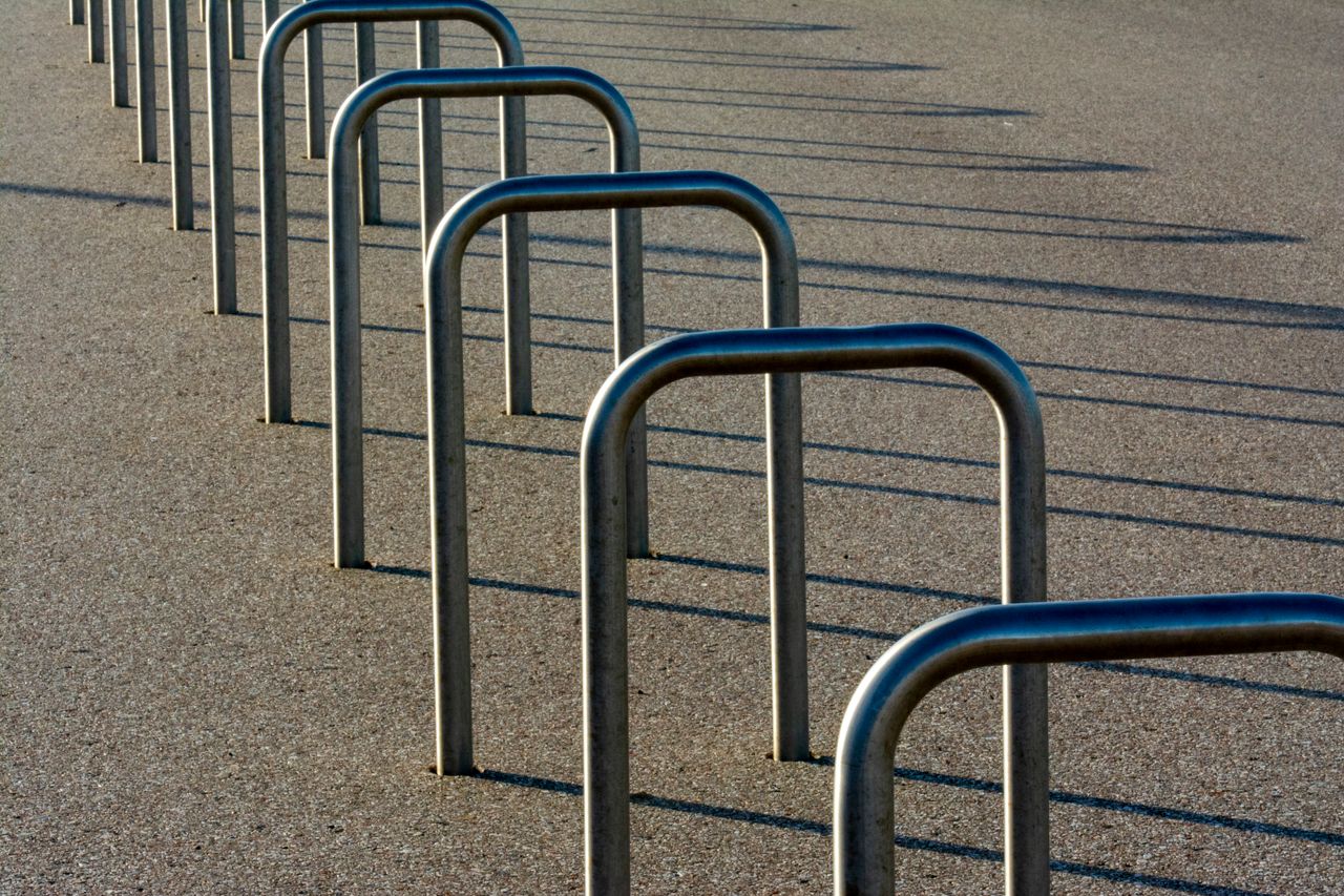 Empty metal bicycle racks casting long shadows on asphalt in urban setting.