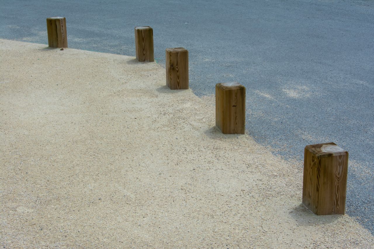 Symmetrical wooden poles on sand and asphalt path, minimalistic urban design.