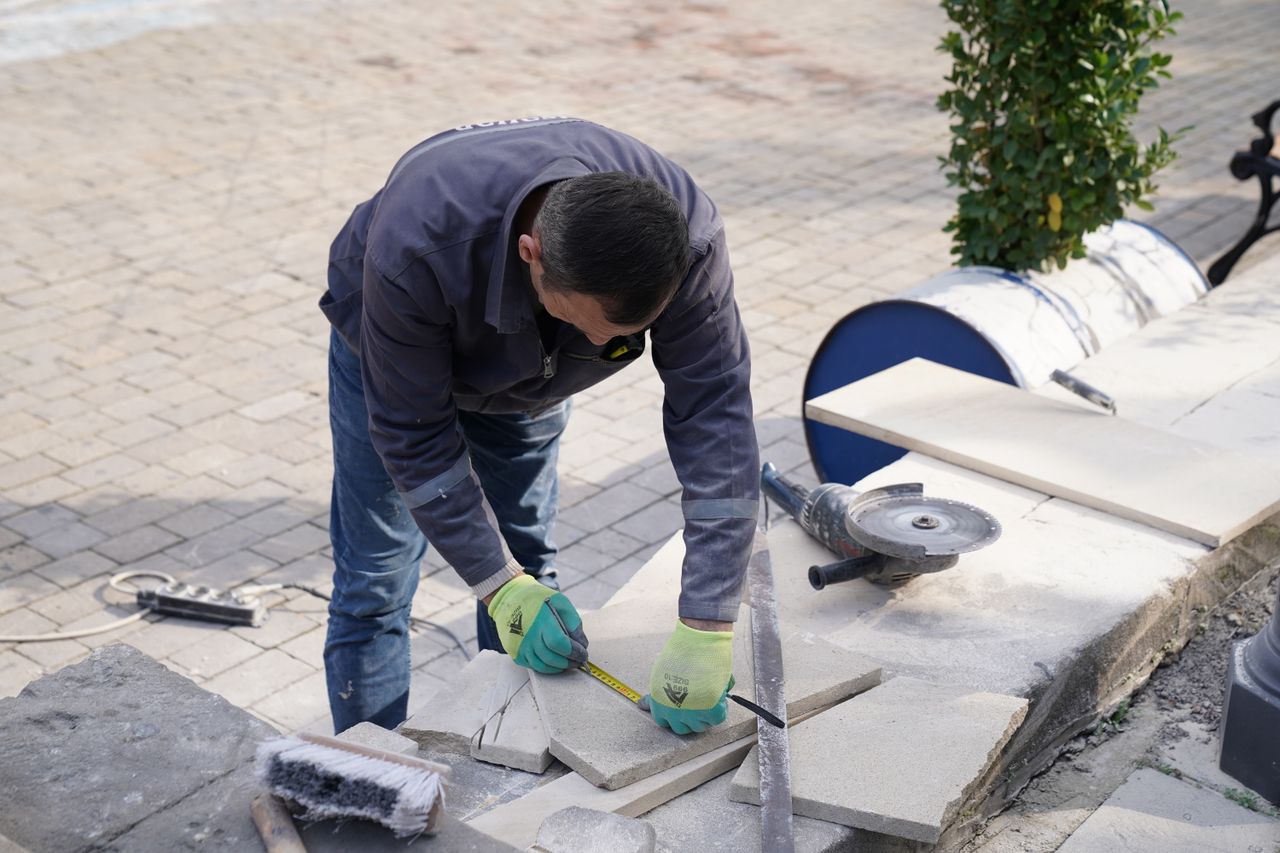 Votre partenaire entretien & maintenance A construction worker measuring tiles outdoors with precision tools.
