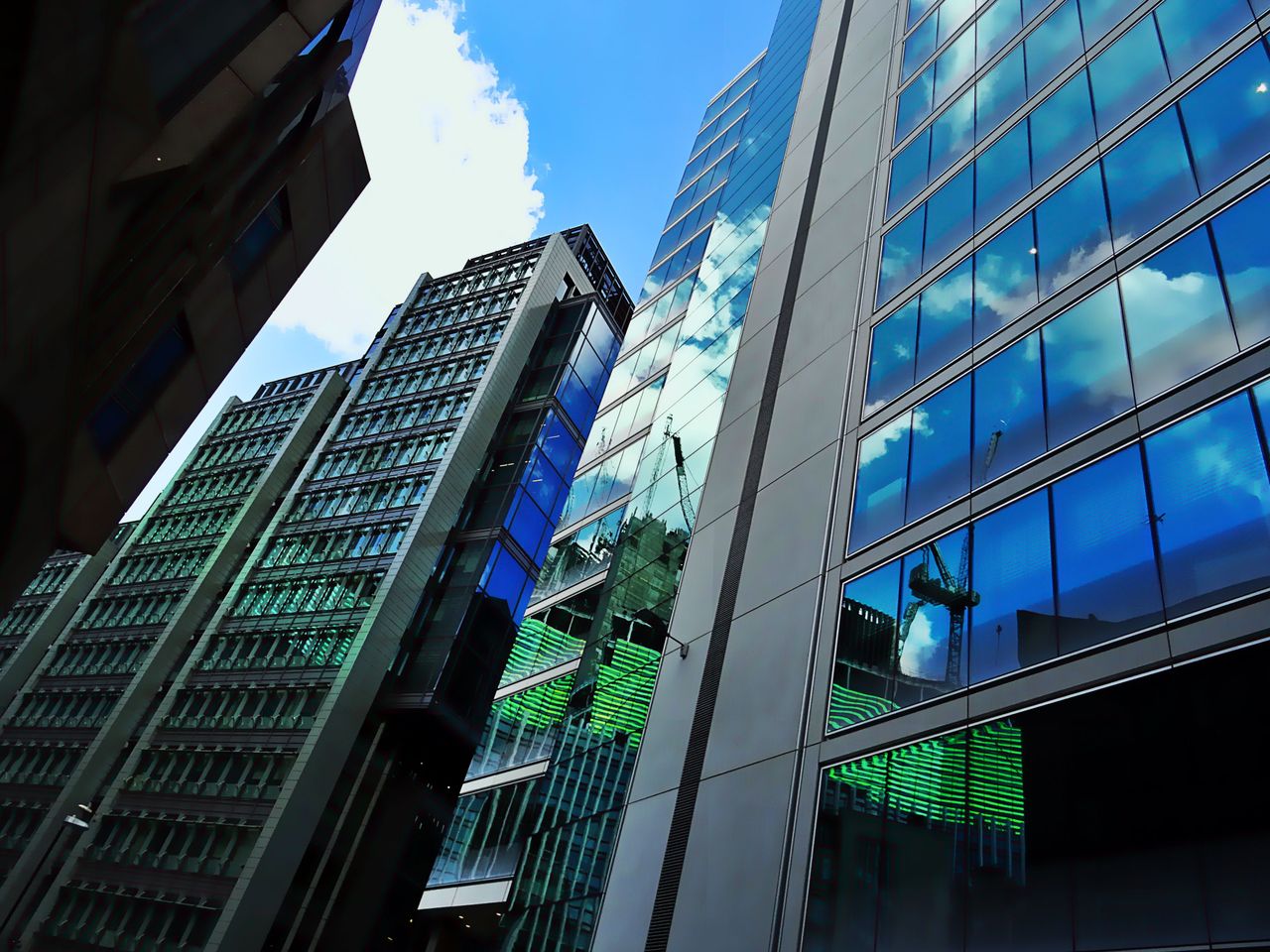 Accueil Low angle view of modern skyscrapers with glass facades reflecting blue sky and clouds.
