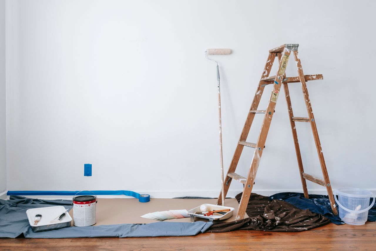 Accueil A room prepared for renovation with a ladder, paint supplies, and drop cloth.